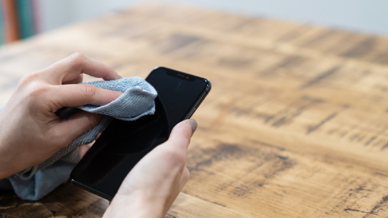Mãos limpando a tela do celular com um pano macio e limpo.
